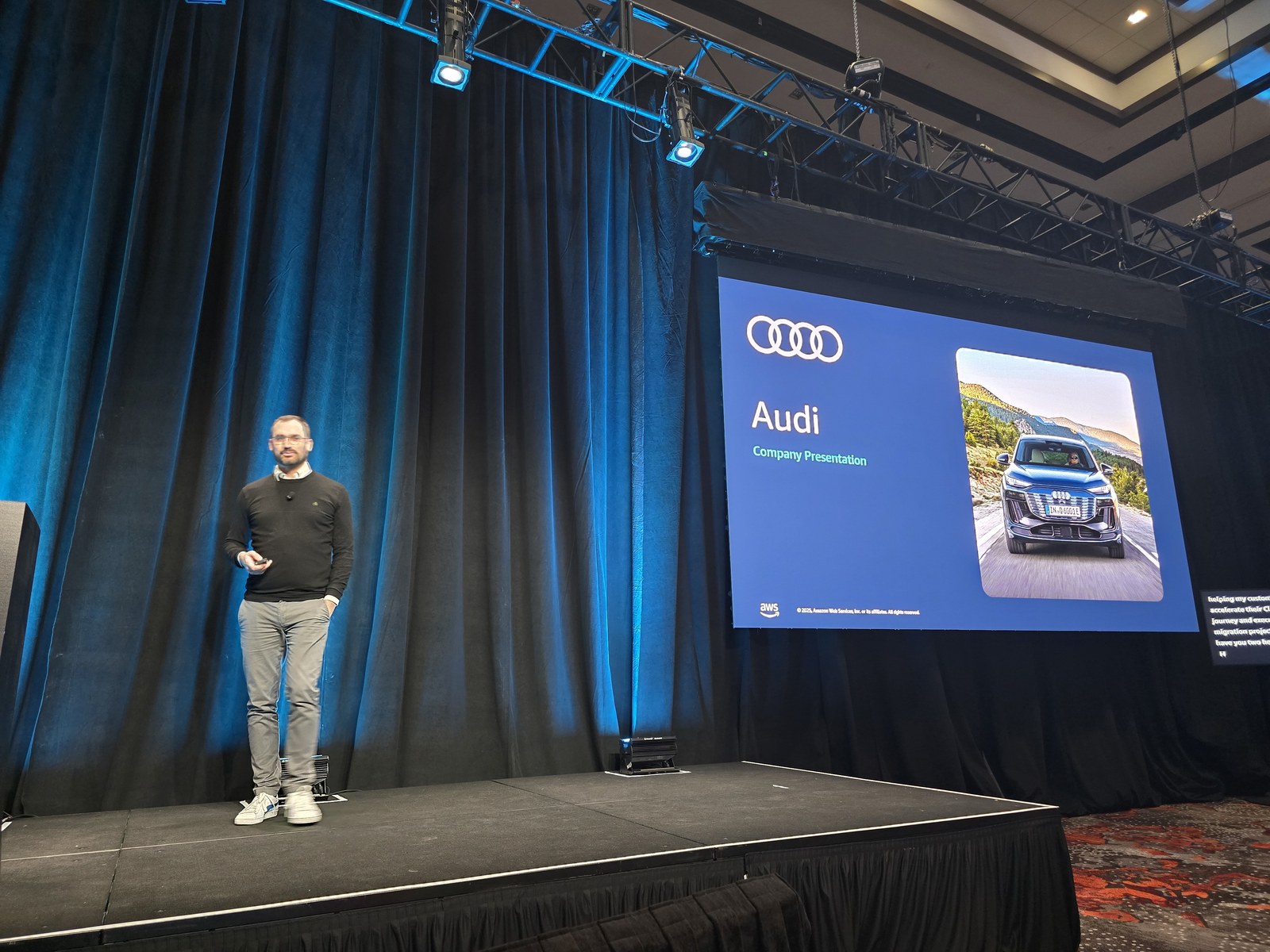 IND367 セッションのステージ。左に立つ Mathias Mayer 氏、右手のスクリーンに Audi の四輪エンブレムと「Audi Company Presentation」の文字、青い SUV の写真が表示されたスライド